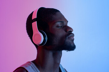 Active lifestyle. Portrait of peaceful black sportsman listening to music in headphones during his training, neon light