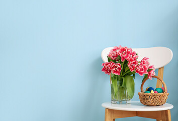 Bouquet of beautiful tulips and basket with Easter eggs on chair near color wall