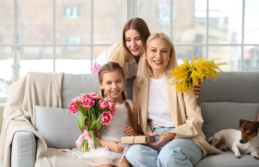 Young woman greeting her daughter and mother with flowers at home on International Women's Day