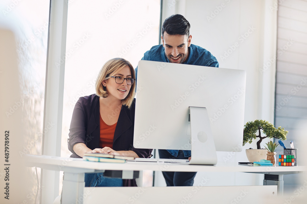 Poster putting technology to work. shot of a young man and woman using a computer together in a modern offi