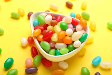 Bowl with different jelly beans on yellow background, closeup