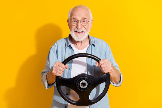 Portrait of attractive cheerful grey-haired man driving rental order buy new vehicle isolated on vivid yellow color background