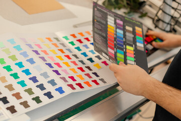 Cropped man hands choosing samples catalog palette rack color advertising T-shirts palette film membrane. Close up - obrazy, fototapety, plakaty