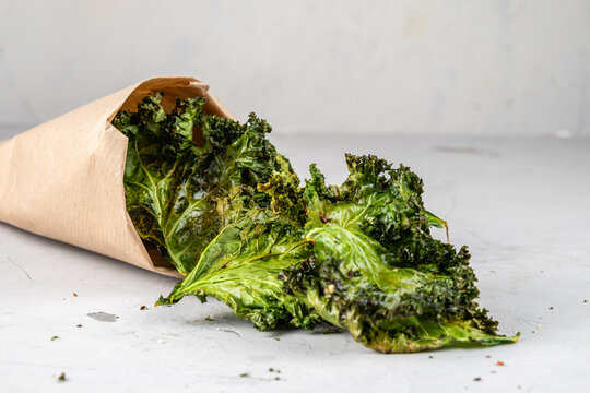 Healthy kale chips in a paper bag on a gray background. A healthy snack of kale chips.