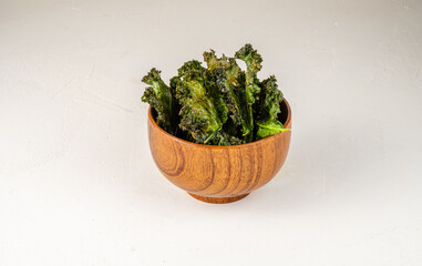 A healthy snack of kale chips in a wooden bowl on a light table. Keto diet.