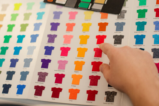Cropped man hand choosing samples templates multicolor advertising T-shirts palette film membrane. Textile production