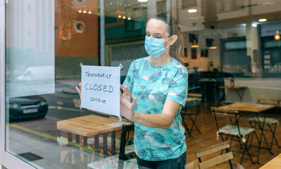 Woman placing a coronavirus closure sign in a coffee shop