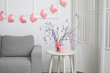 Tree branches decorated with Easter eggs in vase on table near light wall