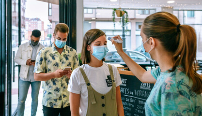 Coffee shop owner checking customers for fever upon entering - obrazy, fototapety, plakaty