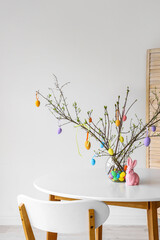 Tree branches decorated with Easter eggs in vase and rabbit on dining table