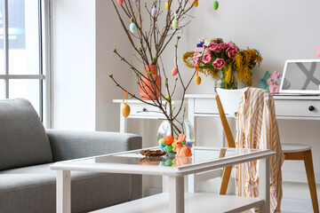 Vase with tree branches, Easter eggs and rabbit on table in living room