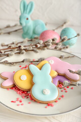 Plate with tasty Easter cookies in shape on bunny and pussy willow branches on table