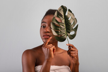 Natural beauty. Beautiful african american woman with smooth skin holding tropical leaf on grey studio background © Prostock-studio