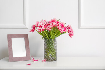 Vase with tulips and blank photo frame on chest of drawers near white wall
