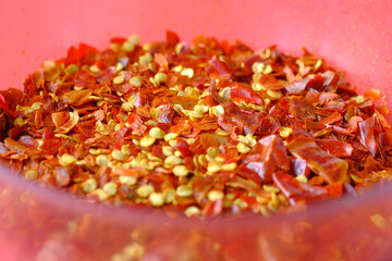 close up of red chili flakes in a bowl on red 