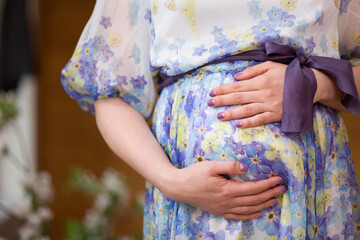 Closeup of young pregnant woman's belly in a beautiful flower violet dress. Expecting a baby. Motherhood and childhood.
