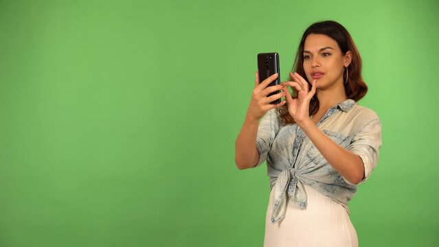 A young beautiful Caucasian woman takes pictures with a smartphone - green screen background