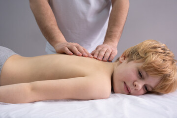The osteopath works with the spine. A teenage child lies on a couch in front of a doctor. A...