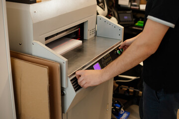 Cropped image man hands using paper cutter machine, guillotine offset. Manufacturing. Control panel, laser cut level. 