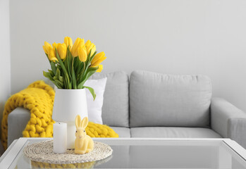 Vase with tulips, candle and Easter rabbit on table in modern living room