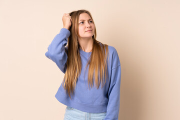 Teenager Ukrainian girl isolated on beige background having doubts while scratching head