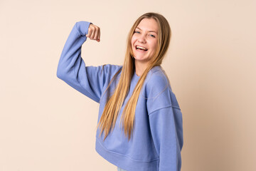 Teenager Ukrainian girl isolated on beige background doing strong gesture