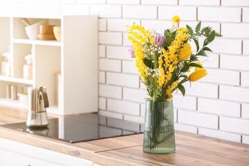 Vase with beautiful flowers on kitchen counter near white brick wall