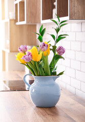 Fototapeta na wymiar Bouquet of tulips on kitchen counter near white brick wall