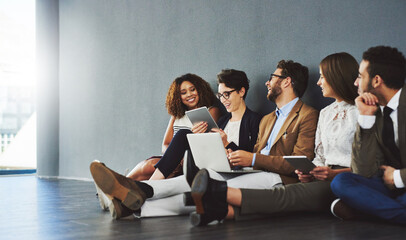 Teamwork makes great work. Studio shot of a group of businesspeople using wireless technology and talking on the floor against a gray wall.