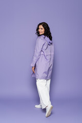 full length of cheerful young woman in violet raincoat on purple.