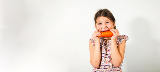 Funny caucasian girl child with carrots on a light background, vegetables and vitamins for children. Strong kid nibbles on a carrot