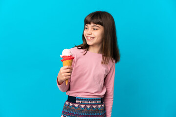 Little girl with a cornet ice cream isolated on blue background looking to the side and smiling