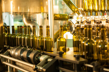 Unlabeled glass bottles in bottling machine at modern winery