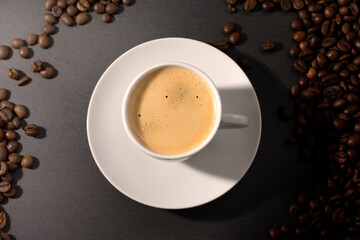 white cup with espresso coffee on a saucer with coffee beans on a dark background