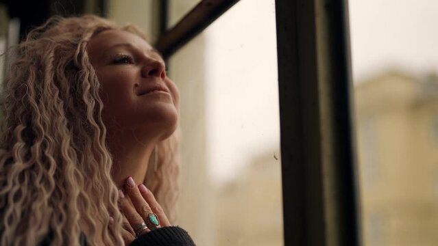 pretty trendy woman with extended blonde hair is looking to window and smiling
