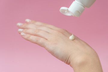 Young hands squeezing cream from tube on pink background. For beauty or medicine products