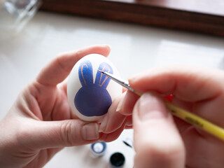 woman paints an Easter egg with paints. Easter bunny drawing on a white egg