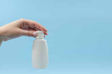 Woman's hand holds white plastic tubes on blue background. Сosmetic bottles for beauty or medicine products