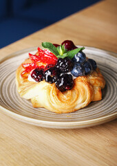 Delicious puff pastry with berries on plate on wood background. Puff pastry with strawberries, cherries, blueberries, blackberries, peaches, pineapple, cranberries and mint. Space for text. Close up.