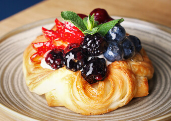 Delicious puff pastry with berries on plate on wood background. Puff pastry with strawberries, cherries, blueberries, blackberries, peaches, pineapple, cranberries and mint. Space for text. Close up.
