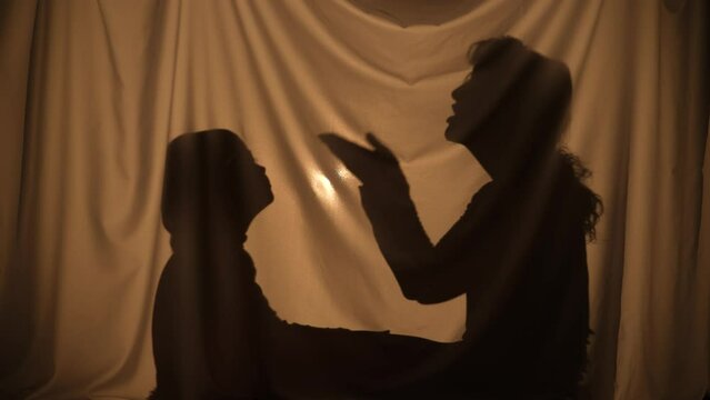 Silhouettes of woman and boy telling stories using shadow play, talking and communication. Mom and little son have fun, sitting behind curtain at home. Puppet theater of shadows. Close up.