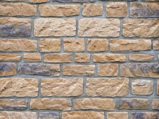 Big stone wall background texture with different colors. Rough weathered surface of a building exterior. Brick pattern of a facade structure with different sized bricks.