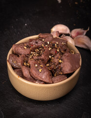 Raw game, beef meat in cubes, in a bowl, on a black background, blackboard, close up. Diced red...