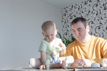 Naklejka premium A dad celebrates Easter with his young son. They beat eggs, eat eggs and have breakfast. Dad teaches the child.