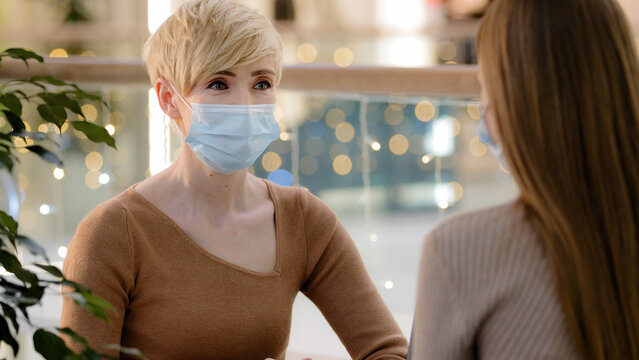 Two Women Friends Mother With Teenage Daughter Talking In Cafe Wear Medical Face Protective Masks. Adult 40s Woman Consultant Advise Client In Pandemic. Middle Aged Lady Talking To Unrecognizable Girl