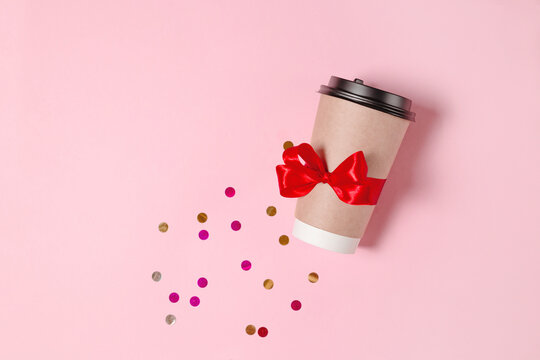 A Brown Paper Cup Of Coffee With A Red Festive Bow On A Pink Flatlay Background. Coffee To Go With Confetti View From Above. Festive Coffee Promotion With A Place For Text.