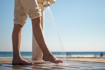 Woman wetting her feet with a shower to clean them from the sand