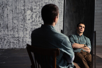 Portrait. Young man with a short hair in a turquoise shirt sit on a chair and looking away in the camera. High quality photo