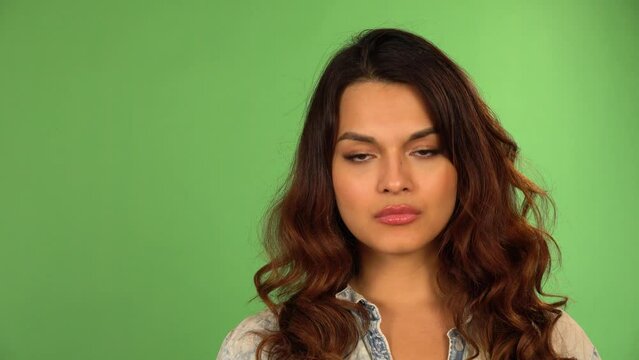 A young beautiful Caucasian woman looks seriously at the camera - closeup - green screen background