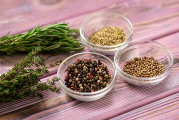 Various spices in glass bowls on a purple wooden background. Black and red pepper, oregano, coriander.